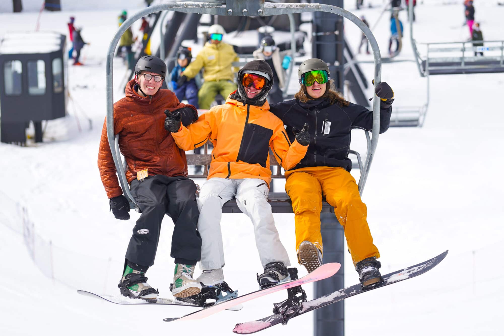 Three snowboarders sitting on a chairlift, smiling at the camera
