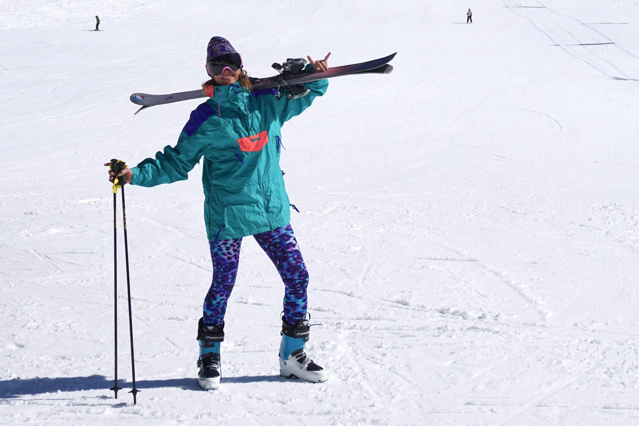 Skier smiling in retro apparel holding a pair of skies and poles.